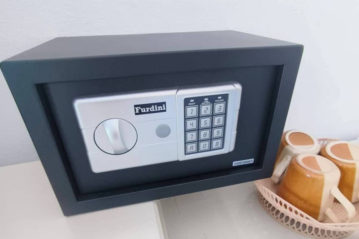 A FurDini safe with a keypad and a lock button, placed on a table next to a basket of mugs.