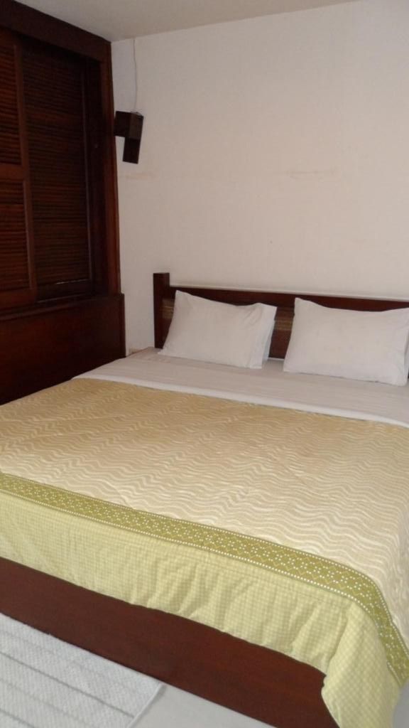 A single bed with a wooden headboard, white bedding, and a decorative border at the foot of the bed.