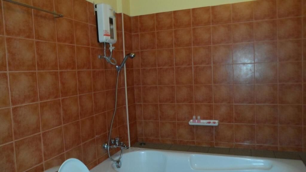 A bathroom with a bathtub, a showerhead, and a soap dispenser on the wall.