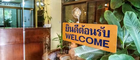 A reception desk with a welcome sign in a foreign language, a water feature, and large green plants.