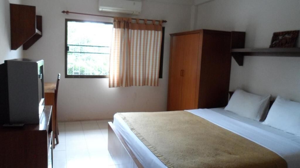 A bedroom with a bed, a wardrobe, a desk with a chair, and a window with curtains.