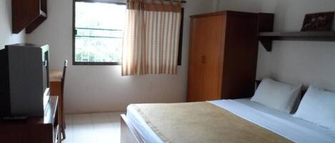 A bedroom with a bed, a wardrobe, a desk with a chair, and a window with curtains.