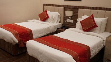 Habitación de hotel con dos camas, cada una con ropa blanca y detalles rojos, una mesita de noche con lámpara y un cabecero de madera.