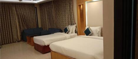 Une chambre d’hôtel avec deux lits simples, un canapé et un ventilateur de plafond.