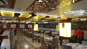 Um restaurante com interior moderno, destacando um teto estampado, lustres e mesas e cadeiras bem organizadas.