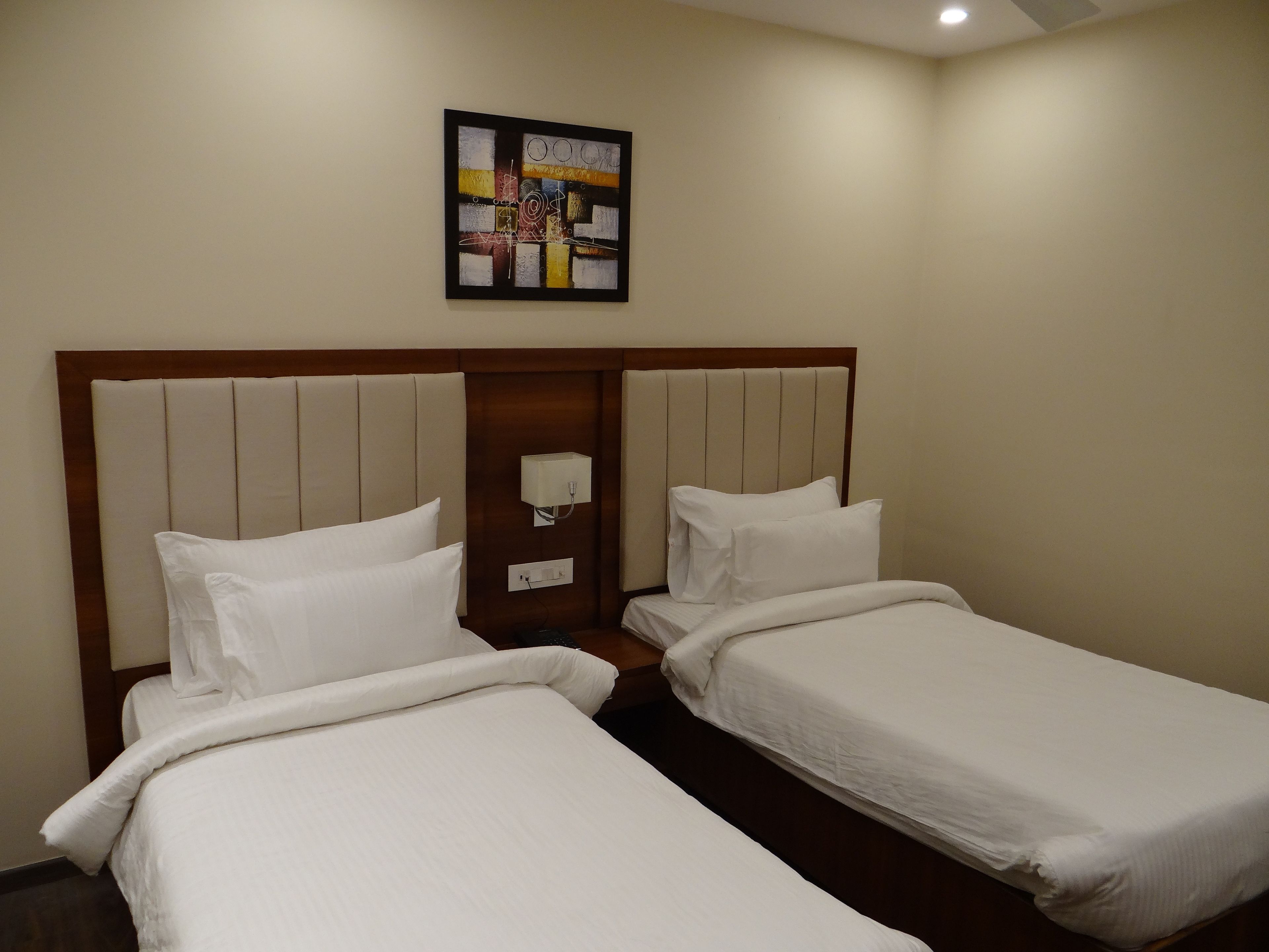 Ein Hotelzimmer mit zwei Einzelbetten, einem Holzkopfteil, einer wandmontierten Lampe und einem gerahmten abstrakten Gemälde.