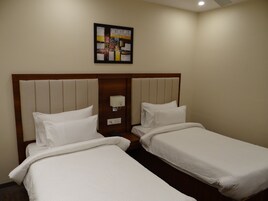 Habitación de hotel con dos camas individuales, cabecero de madera, luz empotrada en la pared y un cuadro abstracto enmarcado.
