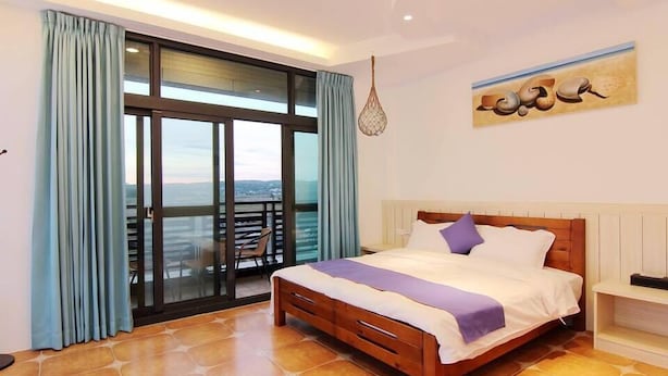A bedroom with a large bed, a balcony with a view, and a hanging light fixture. - Zi Jing Fang lnn (Hengchun)