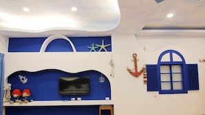 A room with a blue and white color scheme, a flat-screen TV mounted on a blue wall, a small wooden stool, and a window with blue shutters. - Zi Jing Fang lnn (Hengchun)