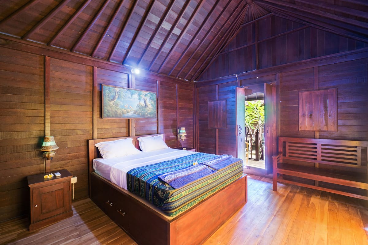 Een houten kamer met een bed, nachtkastje en een schilderij aan de muur.