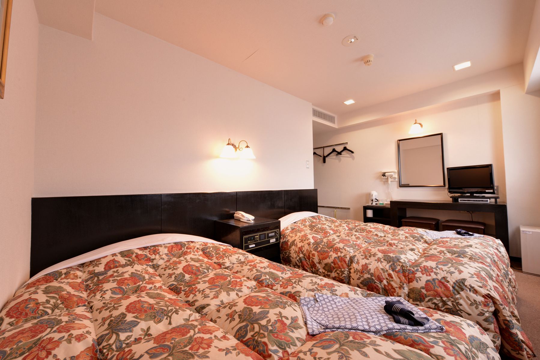 Habitación de hotel con dos camas, un escritorio, un televisor y un espejo.