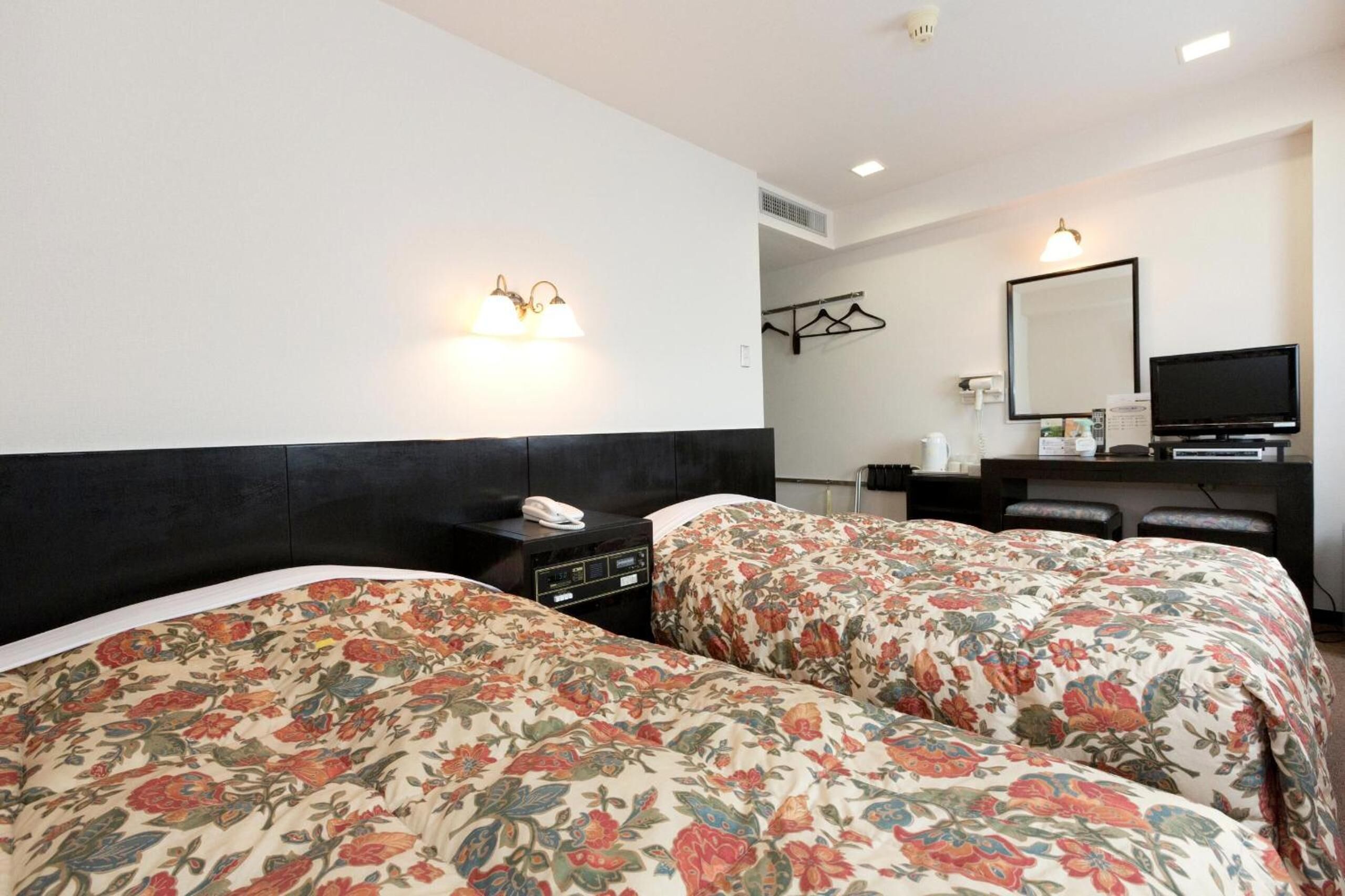 Ett hotellrum med två sängar, ett skrivbord, en TV och en spegel.