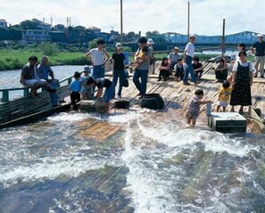 A group of people on a wooden dock by a river with a bridge in the background. - Plaza Hotel Fujinoi (Hita)