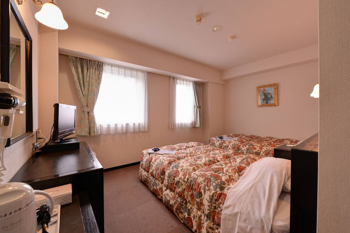 Habitación de hotel con dos camas, un escritorio con computadora, un espejo y una ventana con cortinas.