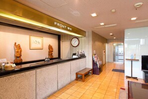 A reception area with a counter, a clock, and a bench. - Plaza Hotel Fujinoi (Hita)