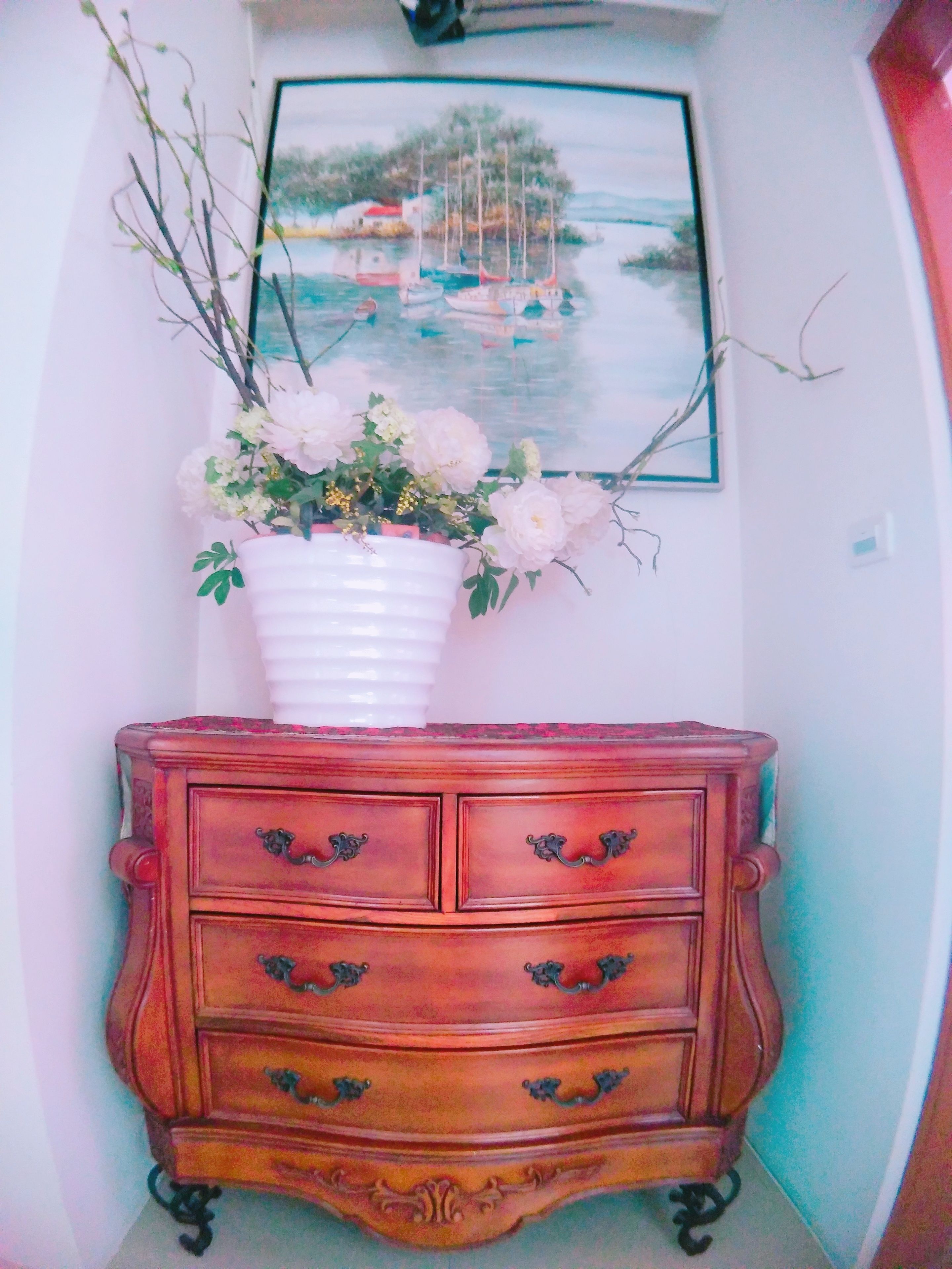Een houten dressoir met sierlijke handgrepen en een witte vaas met bloemen erop.