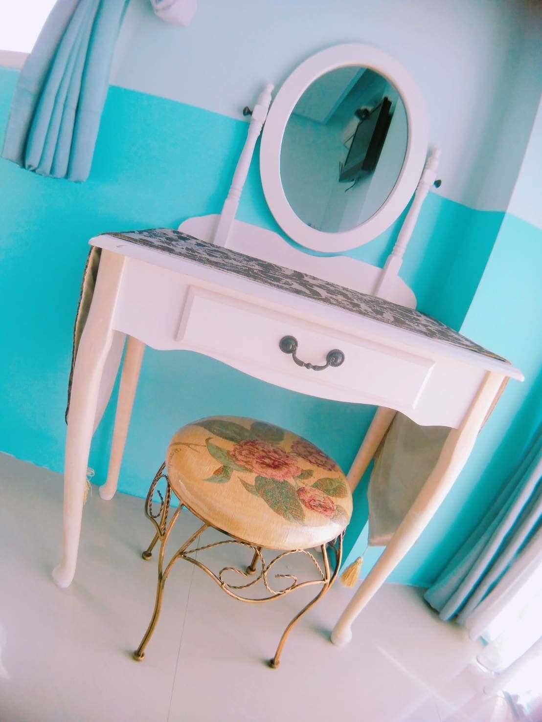 A white vanity with a floral seat and a mirror, set against a turquoise wall.