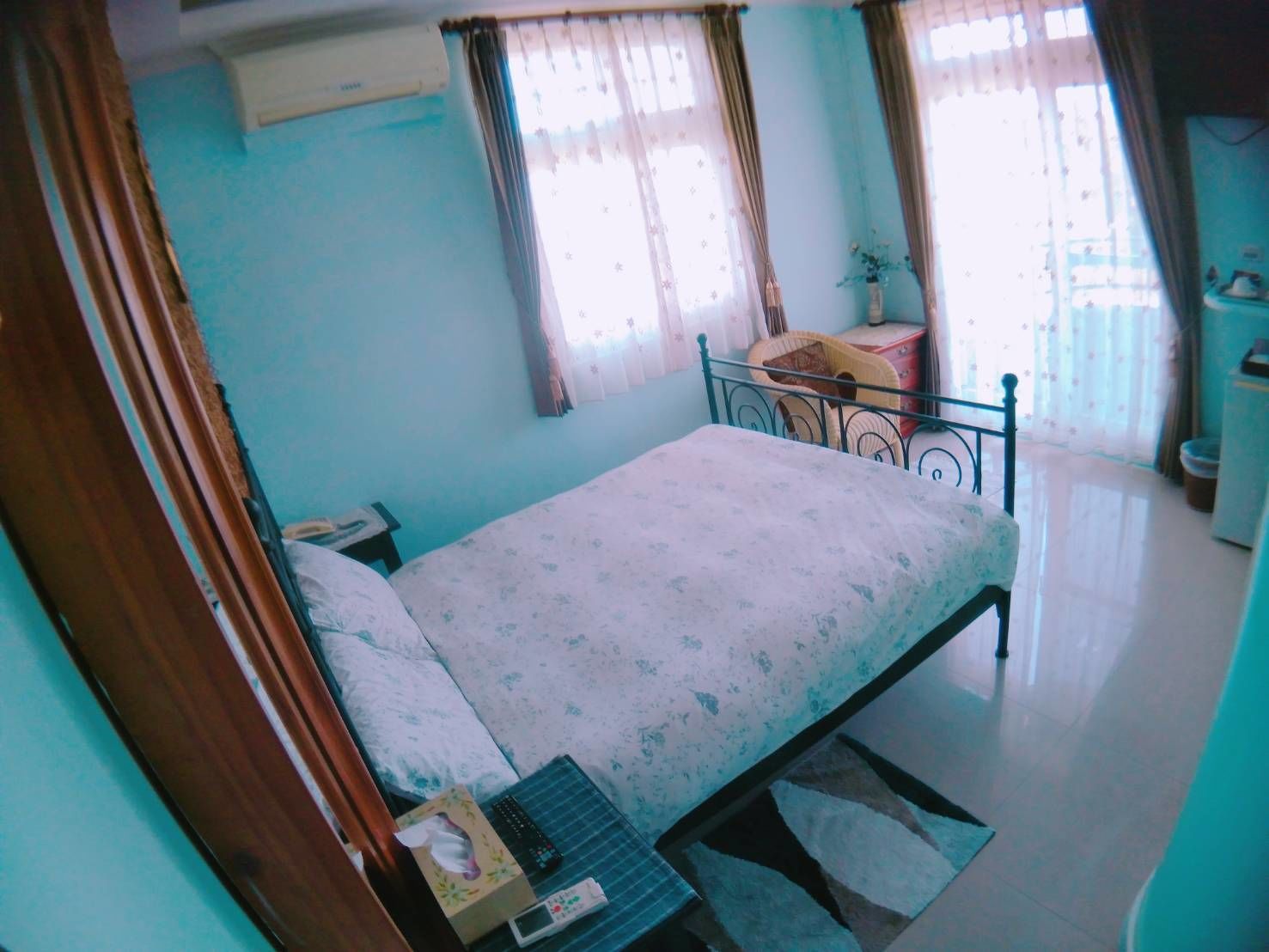 A bedroom with a bed, a bedside table, a chair, a small table, and a window with curtains.