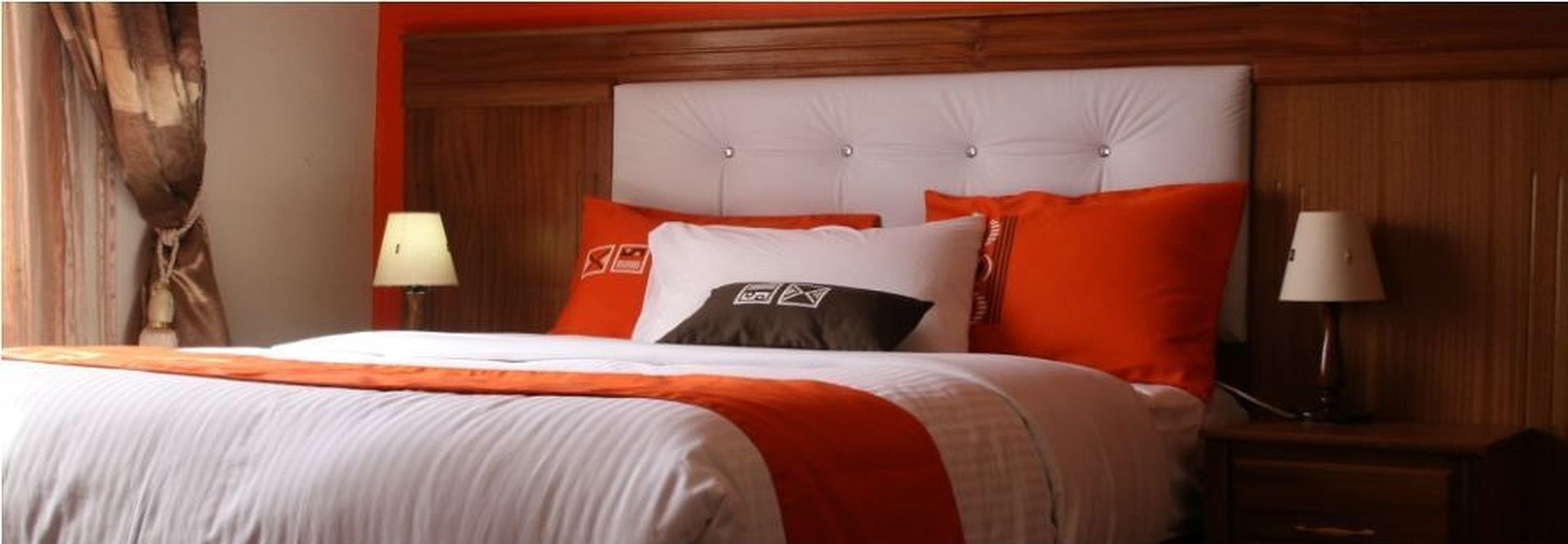 A hotel room with a large bed, orange and white bedding, a wooden headboard, and two bedside lamps.