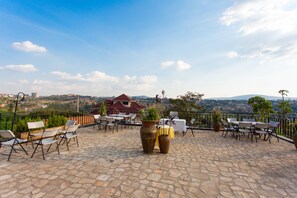 Une terrasse extérieure avec un sol en pierre, des chaises blanches et marron, et des plantes en pot.