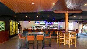 Un espace bar avec différents types de sièges, un comptoir avec un barman et plusieurs téléviseurs diffusant des programmes.