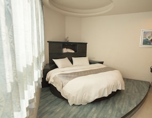 A bedroom with a curved bed, a nightstand, a shelf with a decorative item, and a painting on the wall. - Long Hong B&B (Magong)