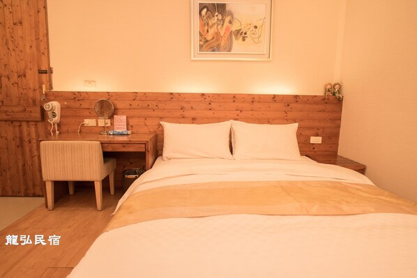 A hotel room with a wooden headboard, a bed with white bedding, a desk with a chair, a mirror, and a small table.