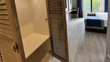 A hotel room with a wooden wardrobe, a bed, a desk, and a view of greenery outside.