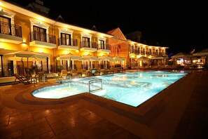 Un hotel con piscina, mobiliario exterior y fachada bien iluminada por la noche.