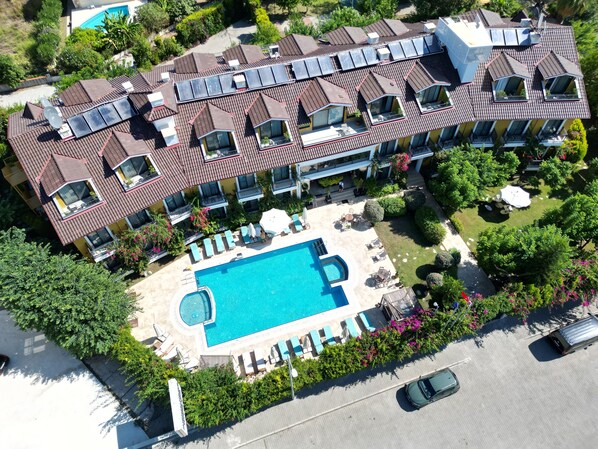 Vista aérea de un hotel con varios balcones, piscina y exuberante jardinería.