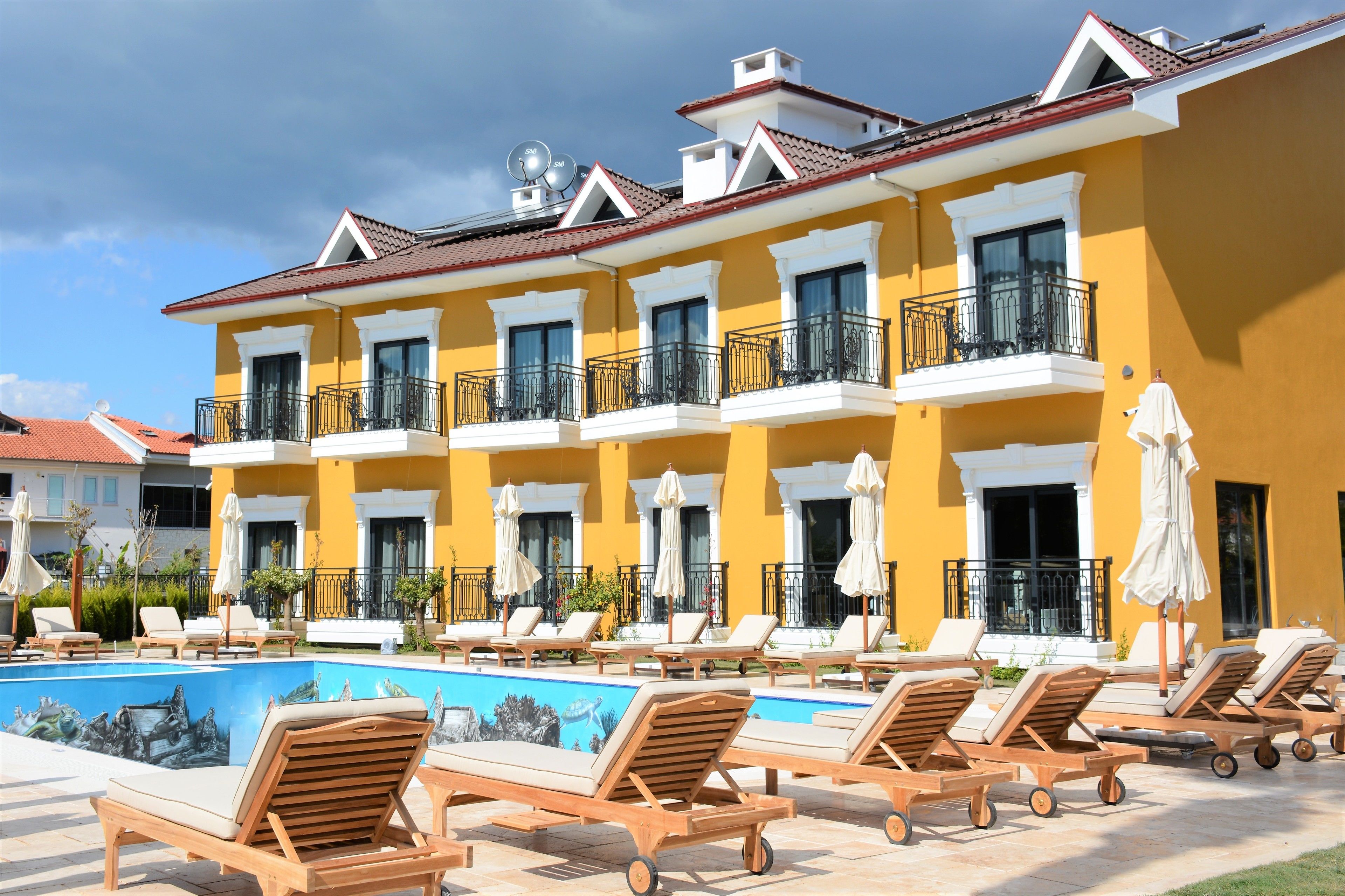 Un hotel con piscina, sillas de descanso y fachada amarilla.