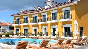 Un hotel con piscina, sillas de descanso y fachada amarilla.