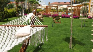 Una hamaca con cojín en un área de césped, rodeada de asientos exteriores y una piscina.