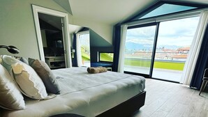 Un dormitorio moderno con una cama grande, una mesita de noche y vistas a la ciudad a través de amplios ventanales.
