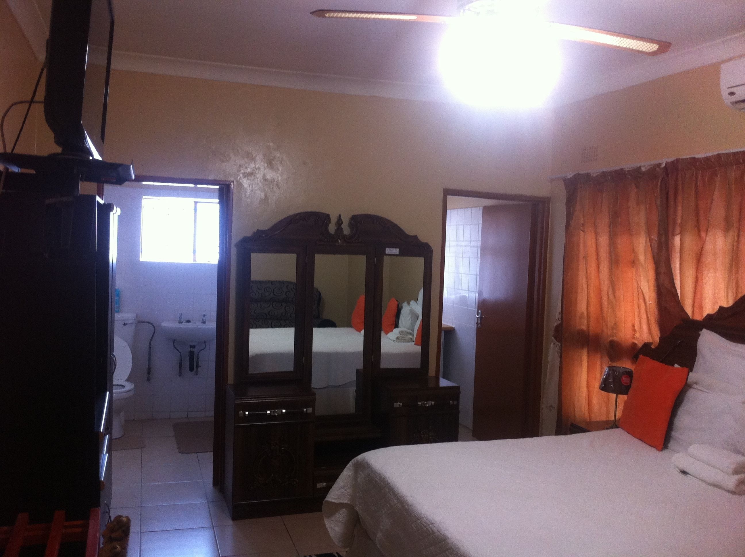 A bedroom with a bed, a dresser, a mirror, a wardrobe, a window, and a bathroom with a toilet and sink.
