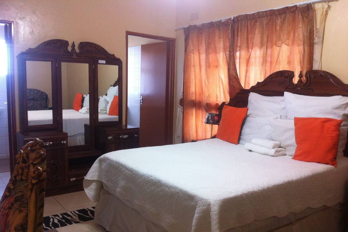 A neatly arranged bedroom with a large bed, a wooden dresser, and a mirror.