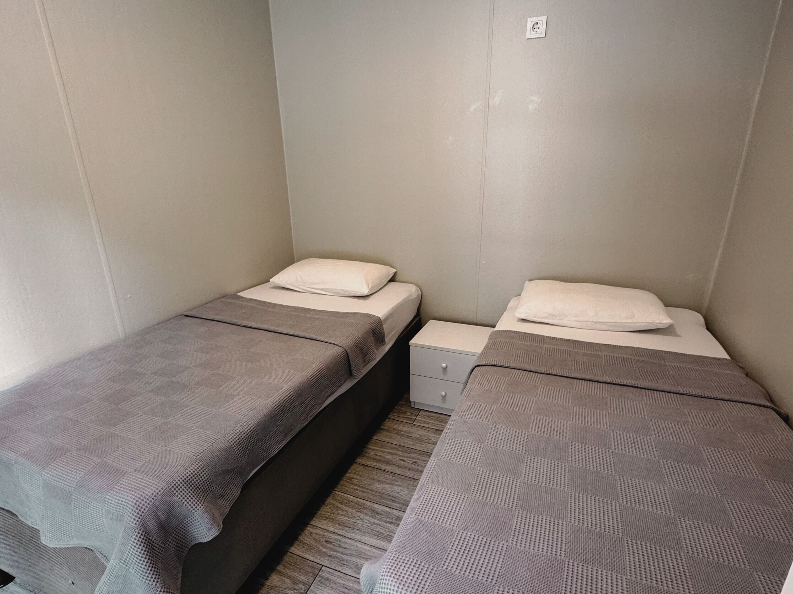 A small, single-room accommodation with two single beds, each with a pillow and a blanket.