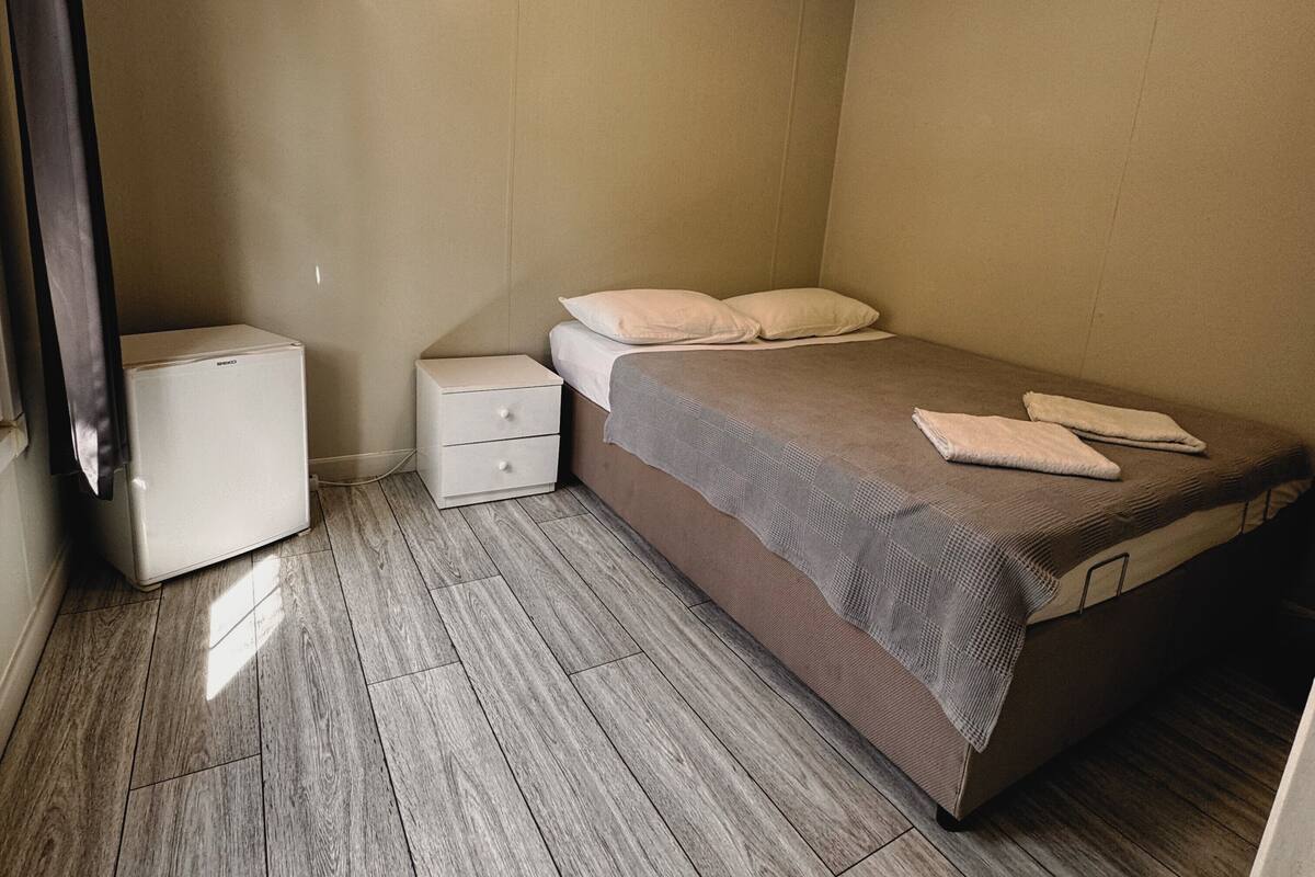 A bedroom with a bed, a nightstand, a small white cabinet, and a heater.