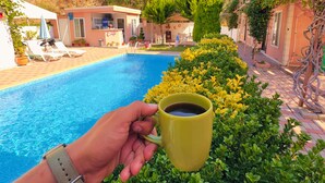 A pool area with a person holding a mug, surrounded by greenery and buildings. - Ali Baba Butik Otel (Marmara)