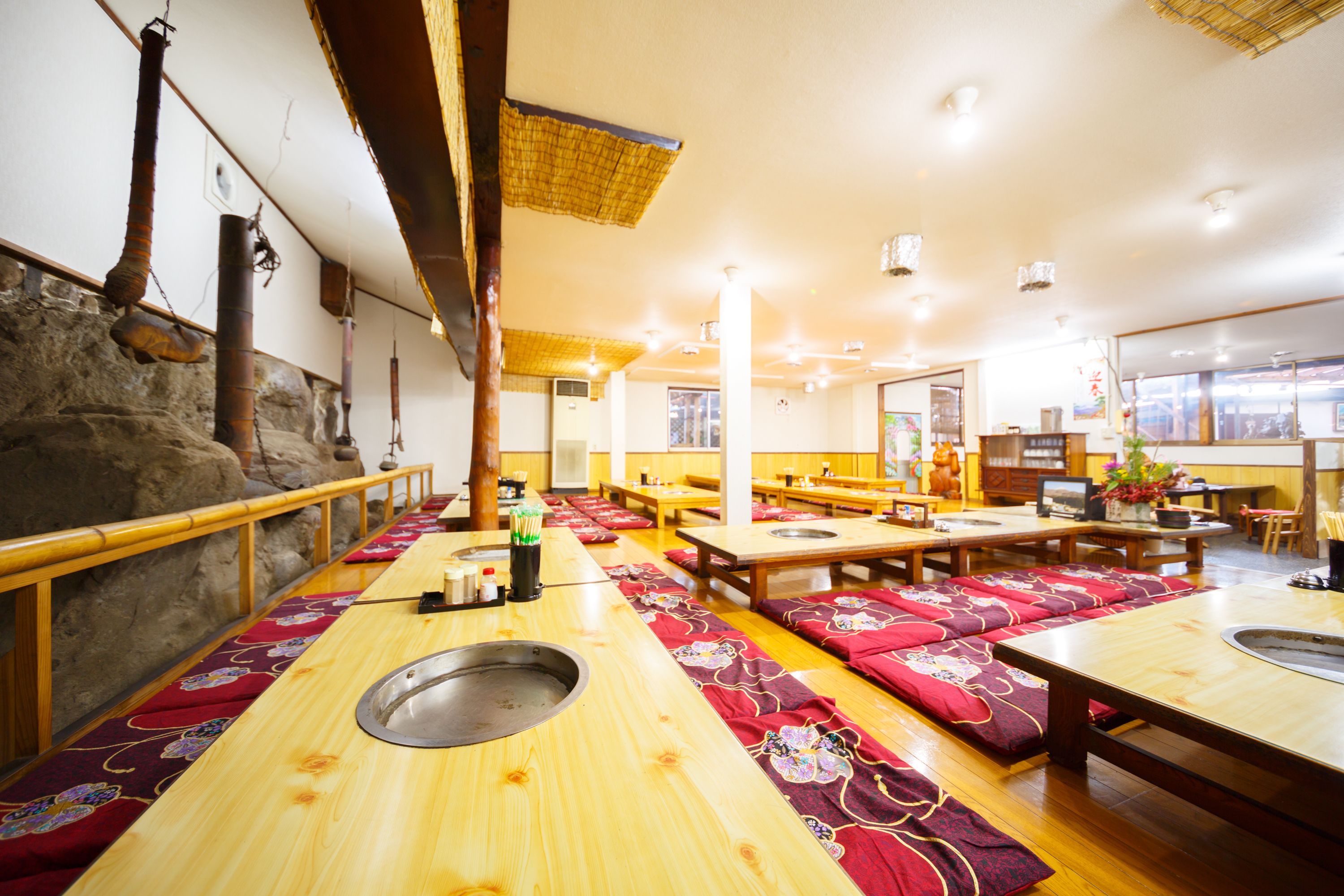 Un restaurante con mesas y bancos de madera, una pared de piedra y un techo tejido tradicional.