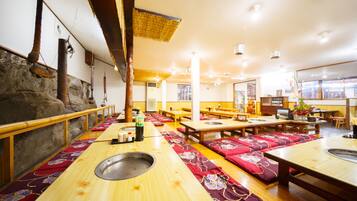 Un restaurante con mesas y bancos de madera, una pared de piedra y un techo tejido tradicional.