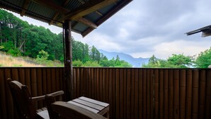 Una terraza de madera con una mesa y sillas, con vista a un área boscosa y montañas distantes.