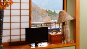 Habitación con televisión sobre una mesa de madera, una lámpara y vista a la montaña a través de una ventana.