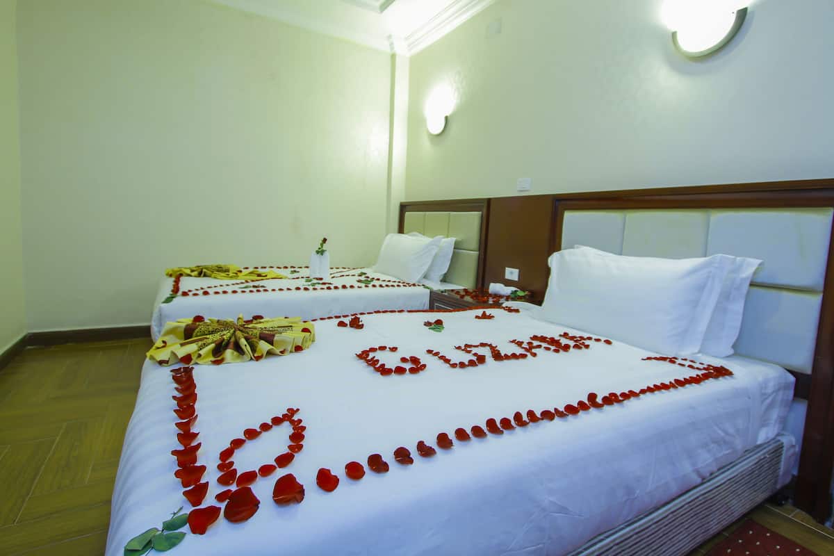 Habitación de hotel con dos camas, cada una decorada con pétalos de rosa y un ramo de flores.