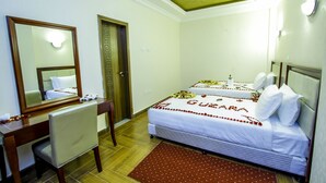 A hotel room with a bed, a desk with a chair, a mirror, and a door. - Guzara Hotel Addis (Addis Ababa)