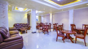 A spacious hotel lobby with leather sofas, wooden dining tables, and chairs, and a chandelier. - Guzara Hotel Addis (Addis Ababa)