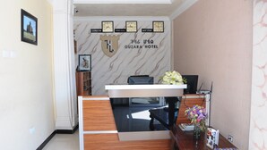 A reception desk with a wooden finish, a black chair, and a vase with flowers. There are clocks on the wall displaying times for London, Addis Ababa, and New York. - Guzara Hotel Addis (Addis Ababa)