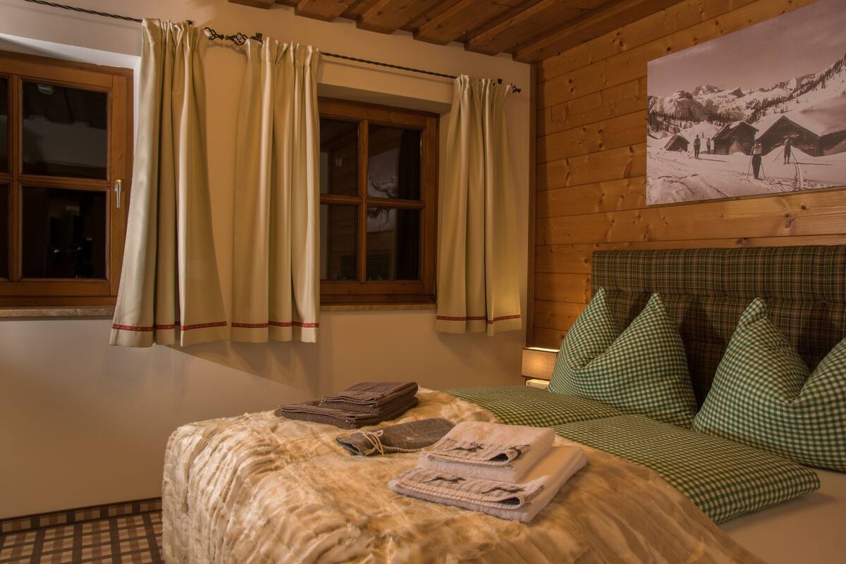 A cozy room with a bed, a window with curtains, a checkered sofa, and a wall-mounted picture.