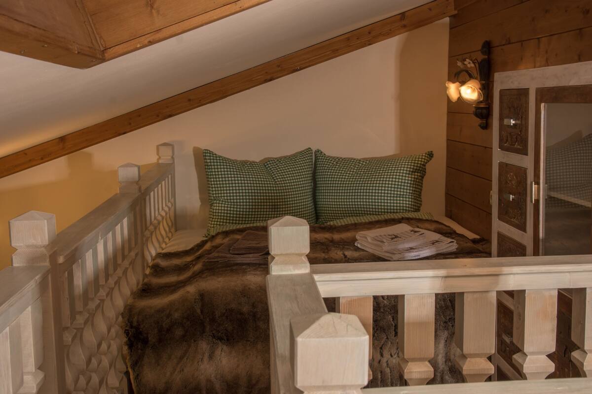 A bedroom with a wooden ceiling, a checkered bedspread, and a fur throw.