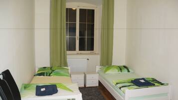 Une chambre avec deux lits, une fenêtre avec des rideaux verts, un radiateur et une petite table.